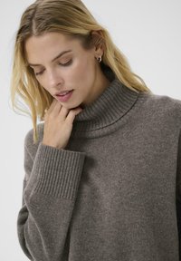 Light brown knitted sweater with a high, ribbed turtleneck and ribbed cuffs; soft texture and relaxed fit.