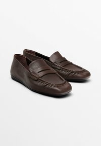 Brown leather loafers with a textured surface, featuring a stitched detail on the toe and a flat sole. Simple design, slip-on style.