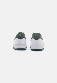 Sneakers Nike Air mają białą skórzaną cholewkę z zielonymi akcentami. Z tyłu znajdują się złote logo oraz teksturowana zielona gumowa podeszwa.