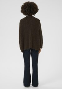 Brown, knit sweater with a loose fit and textured pattern, worn with dark blue flared jeans. Background is plain and white.