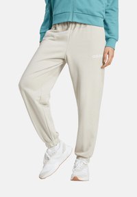Beige sweatpants with elastic cuffs, featuring a white adidas logo on the right leg. Pairing with white athletic shoes.