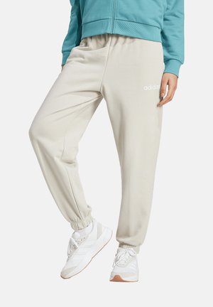 Beige sweatpants met elastische boorden, voorzien van een wit adidas-logo op het rechterbeen. Gecombineerd met witte sportschoenen.