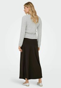 Maglione grigio a maglia con orlo a coste e dettaglio in pizzo, abbinato a una lunga gonna nera fluida e scarpe ballerine argentate. Vista laterale da dietro.