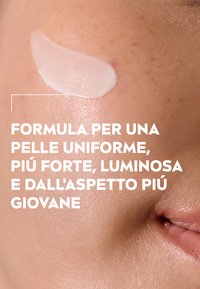 Crema per la cura della pelle bianca applicata su una pelle liscia, che mette in mostra una consistenza leggera e lucida contro un colorito naturale, leggermente macchiato.