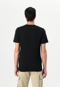 Tricou din bumbac negru cu guler rotund și mâneci scurte, având un design simplu și o croială regulară. Este prezentată doar perspectiva din spate.