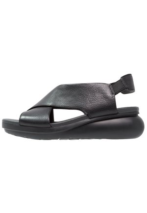 Sandalia de cuero negro con amplias tiras cruzadas, suela acolchada y correa trasera elástica, diseñada para la comodidad y el uso informal.