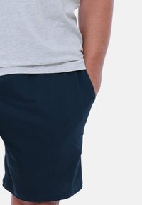 Grau kurzärmliges Shirt mit rundem Ausschnitt, kombiniert mit marineblauen Shorts mit elastischem Bund und seitlichen Taschen.
