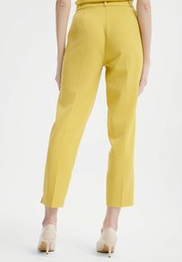 Żółte dopasowane spodnie o prostym kroju, z paskiem w talii i małymi bocznymi rozcięciami na dole, zestawione z jasnobeżowymi szpilkami.