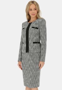 Szary garnitur z tkaniny tweedowej z dopasowaną marynarką z czarnymi akcentami i kieszeniami, zestawiony z ołówkową spódnicą o długości do kolan. Gładka tekstura, strukturalny krój.