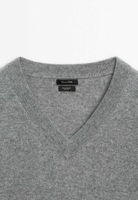 Gray cashmere sweater with a v-neck, featuring a soft texture and ribbed cuffs. Labels indicate 100% cashmere material.