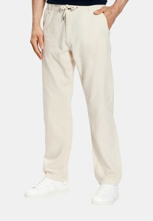 Beige Leinen-Hose mit Kordelzug, getragen von einer Person mit Händen, die nahe der Taschen ruhen, kombiniert mit weißen Sneakers.
