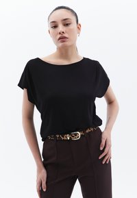 Musta, lyhythihainen t-paita yhdistettynä ruskeisiin korkeavyötäröisiin housuihin, joita korostaa leopardikuvioinen vyö ja hopeinen solki.