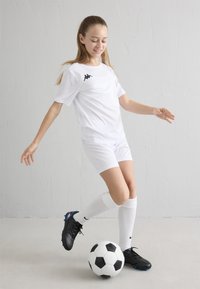 Bela atletska majica in hlače s črnim logotipom, bele nogavice do kolen ter črni nogometni čevlji, zraven pa črno-bela nogometna žoga.