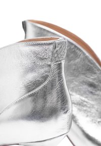 Botines de cuero plateados que presentan una textura suave, un diseño elegante y un detalle trenzado en la parte trasera. Tacón bajo y punta redondeada.
