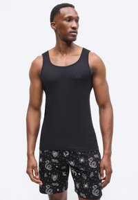 Αθλητικός άνδρας που φοράει εφαρμοστό μαύρο αμάνικο τοπ με το λογότυπο "BOSS" και μαύρο σορτς με λευκά σχέδια εμπνευσμένα από τατουάζ.