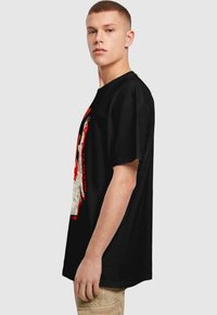Sort kortærmet t-shirt med et rødt og hvidt grafisk design på fronten. Rund udskæring, løs pasform, blødt bomuldsstof.