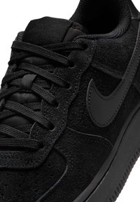 Melnas zamšādas kedas ar teksturētu augšdaļu, melniem auklām un melnu ādas svītru. Iespējas ietver mīkstu apkaklīti un gumijas zoli.