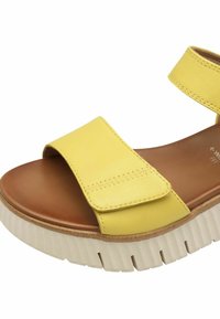 Sandal in pelle gialla con fasce larghe e chiusura in Velcro. Soletta marrone chiaro su un formato spesso e bianco con battistrada. Texture liscia.