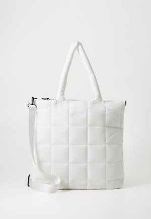 Vadderad vit toteväska med quiltad textur, som har två korta handtag och ett avtagbart axelband. Dragkedjestängning upptill.