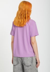 T-shirt lilas à manches courtes avec une coupe décontractée, fabriqué en coton doux. Il dispose d'un col rond et d'une texture lisse.