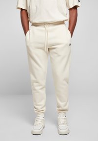 Cremefarvede sweatpants lavet af blødt stof, med snørretalje, sidelommer og et lille logo-detalje på benet.