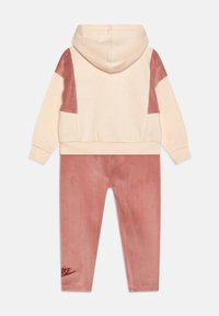 Tuta con cappuccio in crema e rosa pallido. Tessuto morbido, maniche a contrasto, tasca a marsupio e logo ricamato sui pantaloni.