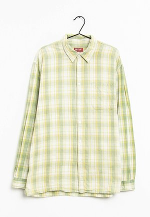 Chemise à manches longues boutonnée, motif à carreaux jaune et vert, suspendue sur un cintre noir sur fond blanc.