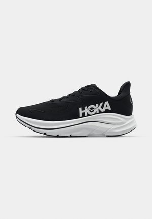 Svart atletikksko med teksturert overdel, hvit logo, polstret såle og en strømlinjeformet, rund design. Har snøresystem og kontrastdetaljer.