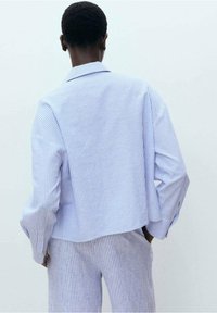 Chemise à rayures bleu clair et blanc avec des boutons, coupe décontractée et manches longues, dotée d'un empiècement au dos et d'épaules tombantes.