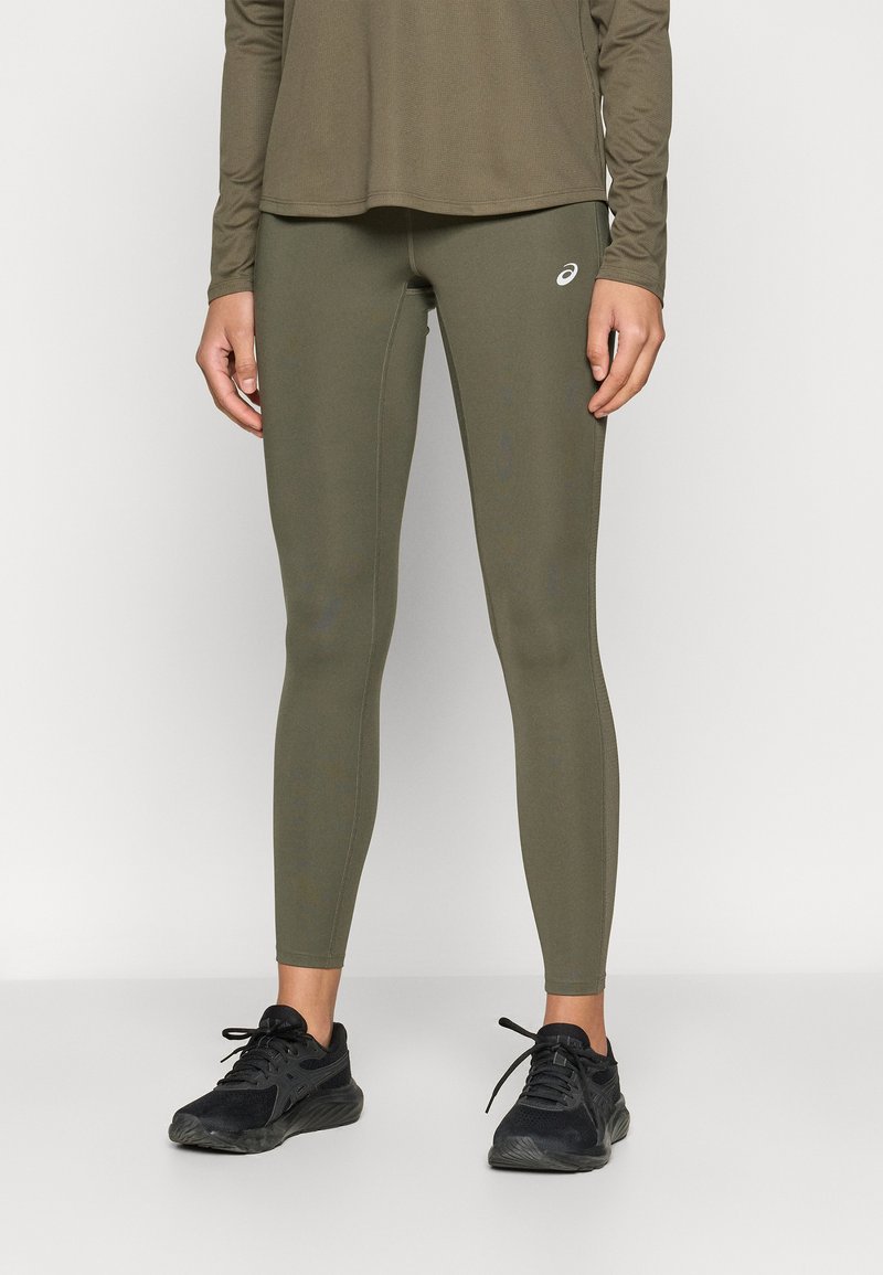 Φυστικί αθλητικό κολάν με λείο υφή και εφαρμοστή σχεδίαση· διαθέτει ένα μικρό λευκό λογότυπο στον γαστροκνήμιο. Συνδυασμένο με μαύρα αθλητικά παπούτσια.