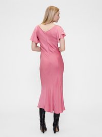 Rozā satīna midi kleita ar īsām izplešanās piedurknēm, V formas aizmuguri un pieguļošu siluetu, apvienota ar melnām ceļgala augstām stiletto zābakiem.