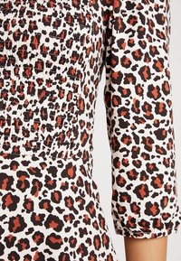 Top z nařasené látky s leopardím potiskem v černé, hnědé a rezavé barvě na bílém pozadí. Rukávy jsou ohrnuté na tříčtvrteční délku.