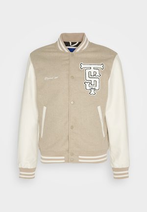 Beige-witte varsityjas met drukknoopsluiting, gestreepte boorden en kraag, twee voorzakken en geborduurde logopatches op de borst.