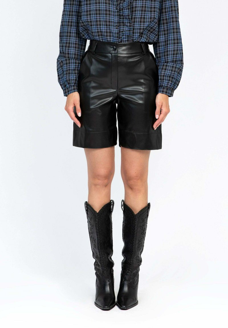 Un short en cuir noir avec une taille haute et une finition lisse, associé à des bottes de cowboy noires détaillées et une chemise à manches longues en plaid bleu.