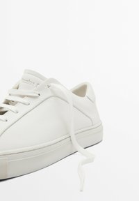 Hvide lædersneakers med rund tå, flade snørebånd og en struktureret sål. Minimalistisk design med et diskret logo på tungen.