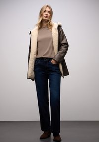 Braune Lederjacke mit cremefarbenem Lammfellkragen, beigem Oberteil, blauen Jeans mit geradem Bein und braunen Stiefeletten. Schlichtes Design, neutrale Farben.