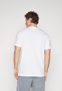 Hvid crew-neck t-shirt lavet af bomuld, korte ærmer og en afslappet pasform. Ingen synlige logoer eller mønstre. Parret med grå shorts.