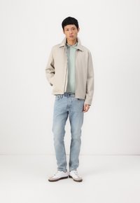 Light beige jacket, mint green polo, light blue jeans, and white sneakers with gray accents. Simple design and smooth texture throughout.