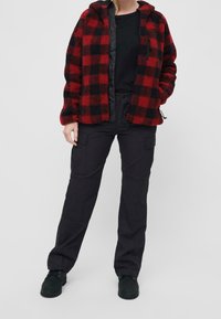 Czerwona i czarna polarowa kurtka w kratę z kapturem, zestawiona z czarnymi spodniami typu cargo. Miękka tekstura, zamek błyskawiczny oraz wiele kieszeni w spodniach.
