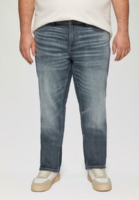 Ciemnoniebieskie dżinsy o prostym kroju, z wyszczotkowanym wykończeniem, pięcioma kieszeniami i przeszyciami, zestawione z jasnymi trampkami.