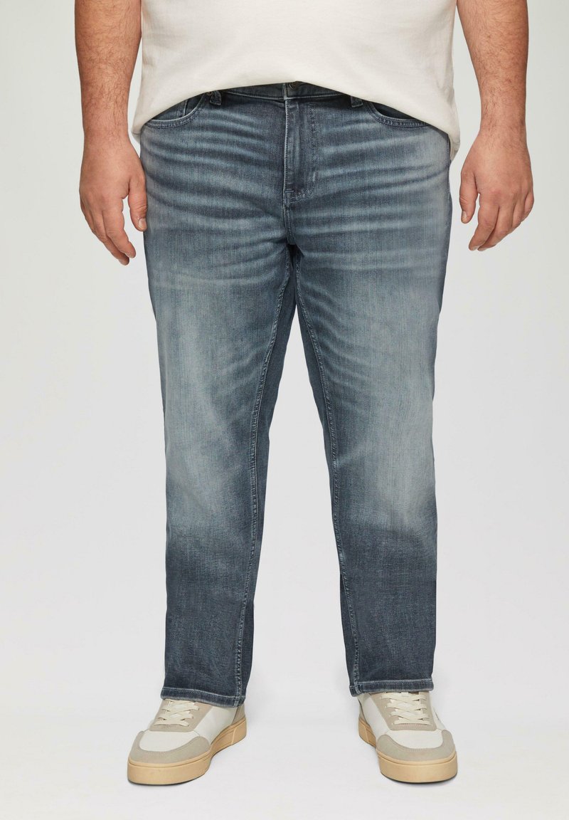 Ciemnoniebieskie dżinsy o prostym kroju, z wyszczotkowanym wykończeniem, pięcioma kieszeniami i przeszyciami, zestawione z jasnymi trampkami.