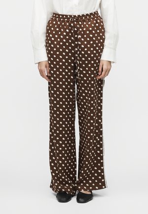 Brown wide-leg pants with white polka dots and side trim, worn with a white long-sleeve shirt and black shoes.