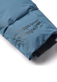 Sininen tilkkukangas, jossa on ruudukkomalli; sisältää tummanharmaalla painettua tekstiä. Musta neuloskumin reunassa. Pehmeä tekstuuri.