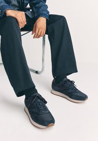 Baskets bleu marine avec panneaux en daim et tissu, semelles en caoutchouc et lacets ronds. Présentent un accent contrastant tan sur le talon.