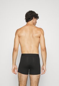 Schwarze Baumwoll-Boxershorts mit einem weichen elastischen Bündchen, in Oberschenkelhöhe und mit einer glatten Textur. Keine sichtbaren Muster oder Akzente.