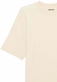 Krémové bavlněné tričko s kulatým výstřihem, krátkými rukávy a minimalistickým designem se malým logem poblíž límce.