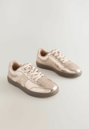 Metaliczne trampki w różowym złocie o fakturowanym wykończeniu, okrągłym czubku, płaskich sznurowadłach i gumowej podeszwie. Panele boczne mają subtelny detal w designie.