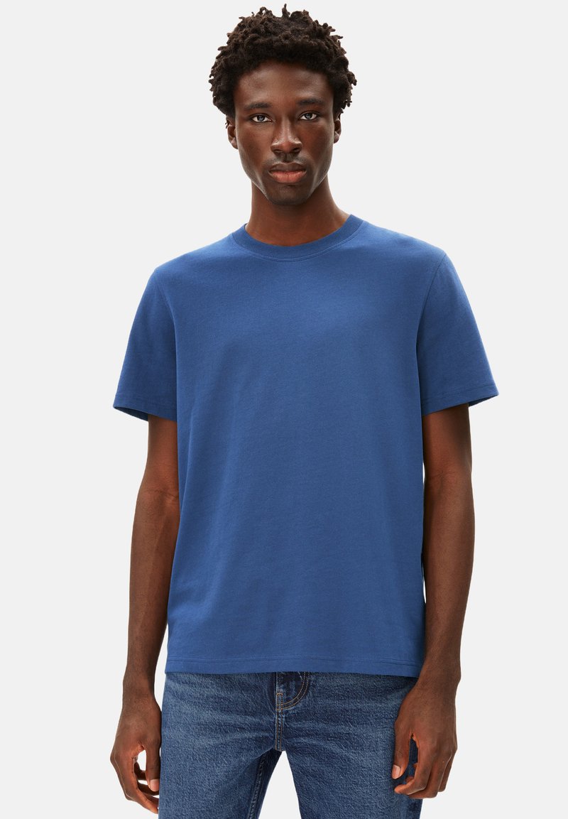 T-shirt en coton bleu avec un col rond, des manches courtes et une coupe décontractée, associé à un jean en denim bleu. Pas de logos ou de motifs visibles.