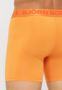 Narancssárga, testhezálló boxer alsó, sima textúrával és kontrasztos narancssárga derékszíjjal, amelyen vastag betűkkel "BJÖRN BORG" felirat található.
