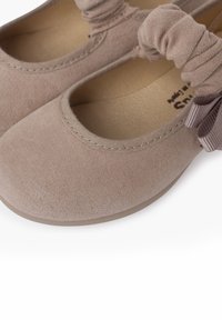 Bailarinas de color beige claro con una parte superior de tela suave, detalles elásticos alrededor del tobillo y un acento de cinta decorativa.